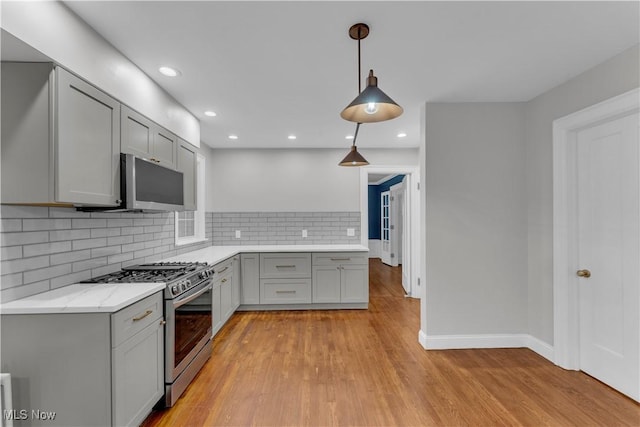 kitchen with decorative light fixtures, gray cabinetry, backsplash, light hardwood / wood-style floors, and stainless steel gas range oven