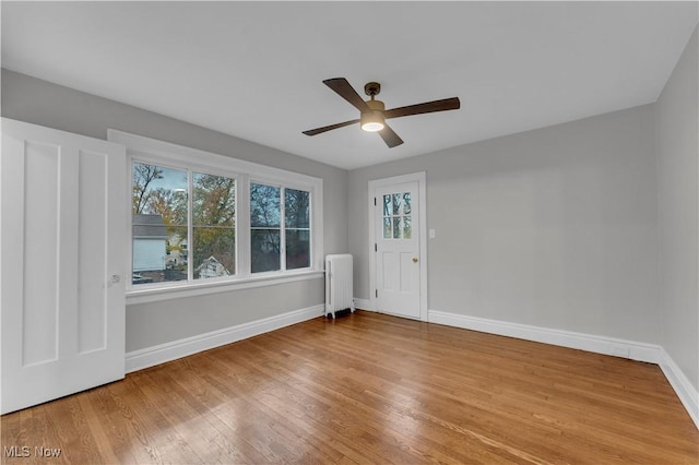 empty room featuring hardwood / wood-style flooring, radiator heating unit, ceiling fan, and plenty of natural light