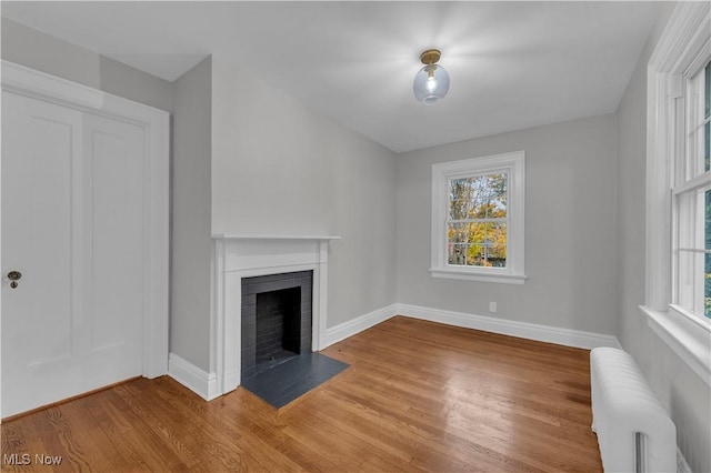 unfurnished living room with a healthy amount of sunlight, a brick fireplace, radiator heating unit, and wood-type flooring