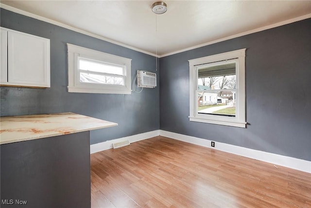 spare room with crown molding, a wall mounted AC, a healthy amount of sunlight, and light wood-type flooring