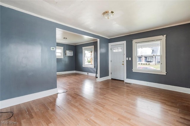 entrance foyer with ornamental molding, a wall unit AC, and light wood-type flooring