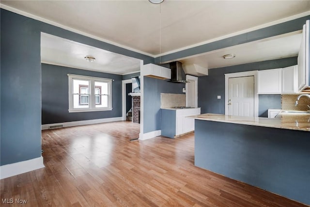 kitchen featuring wall chimney range hood, white cabinets, and light wood-type flooring