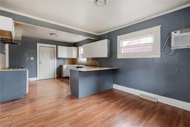 kitchen with an AC wall unit, kitchen peninsula, light hardwood / wood-style flooring, and white cabinets