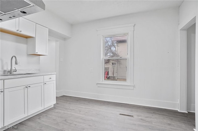 kitchen with ventilation hood, white cabinetry, sink, and light hardwood / wood-style floors