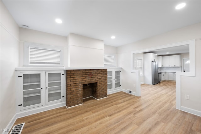 unfurnished living room featuring light hardwood / wood-style floors and a brick fireplace