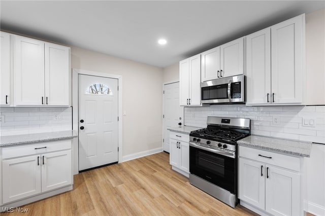 kitchen with light hardwood / wood-style flooring, appliances with stainless steel finishes, white cabinetry, light stone countertops, and decorative backsplash