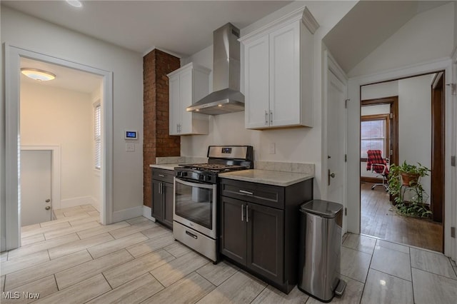 kitchen with stainless steel gas range oven, wall chimney range hood, and white cabinets