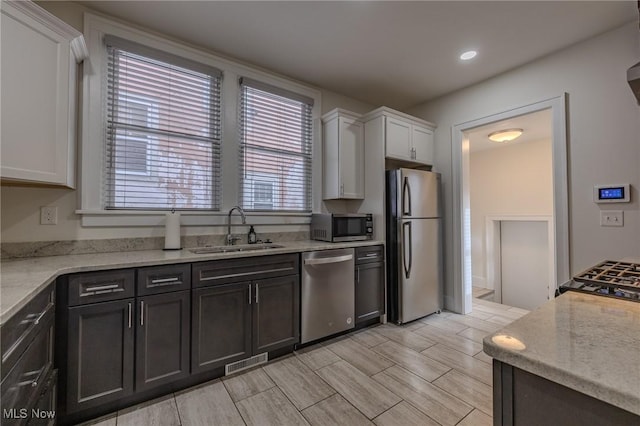 kitchen featuring light stone counters, stainless steel appliances, sink, and white cabinets