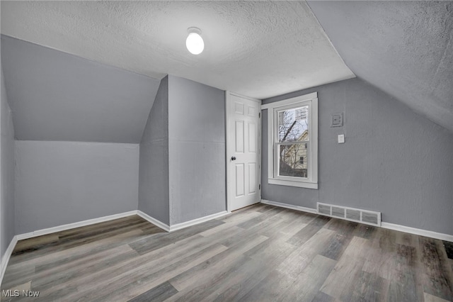 additional living space featuring lofted ceiling, hardwood / wood-style floors, and a textured ceiling