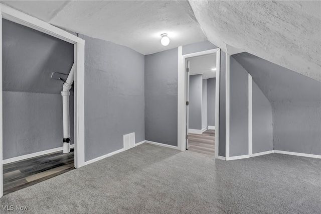 additional living space featuring dark colored carpet, lofted ceiling, and a textured ceiling