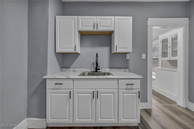 kitchen featuring light stone countertops, sink, white cabinets, and light wood-type flooring