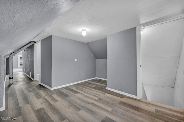 additional living space with lofted ceiling, hardwood / wood-style floors, and a textured ceiling