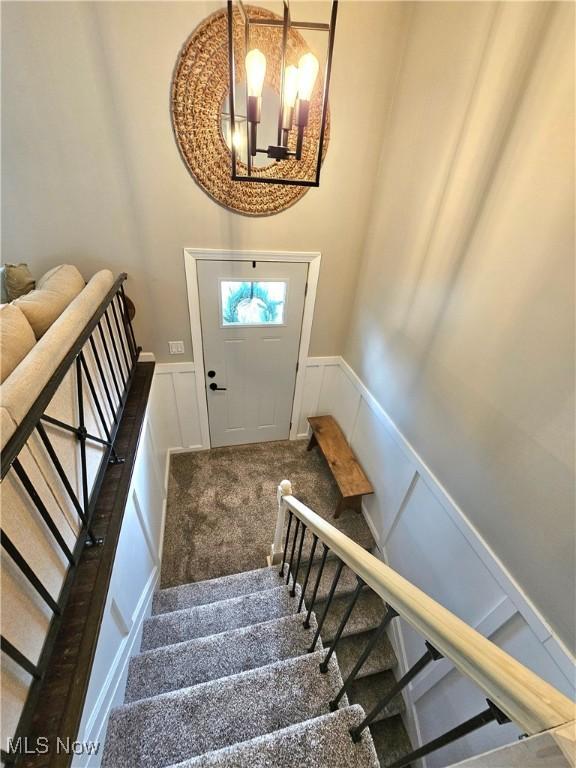 stairs with an inviting chandelier and carpet floors