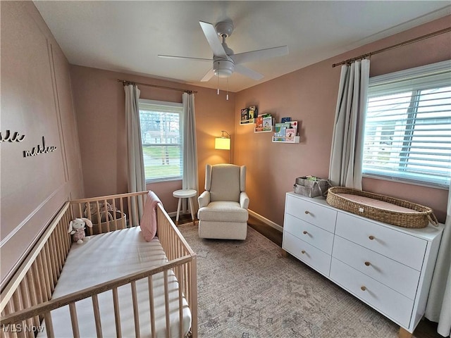 bedroom with a nursery area, ceiling fan, light carpet, and multiple windows