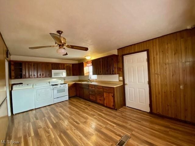 kitchen featuring wood walls, separate washer and dryer, sink, white appliances, and light hardwood / wood-style flooring