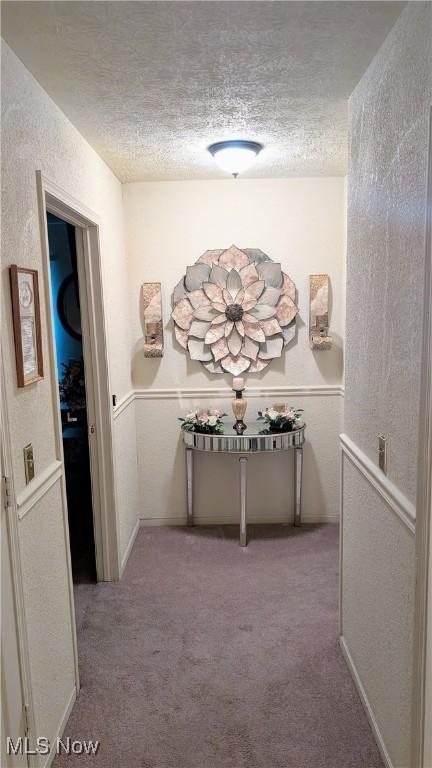 hallway with light carpet and a textured ceiling