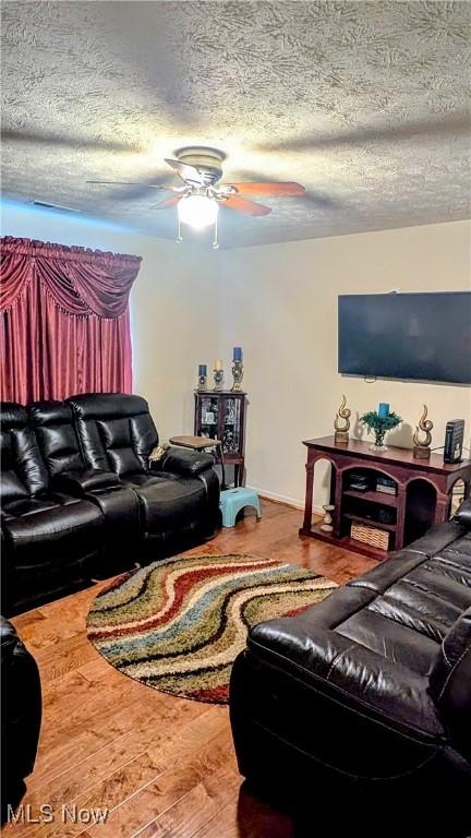 living room featuring ceiling fan, hardwood / wood-style floors, and a textured ceiling