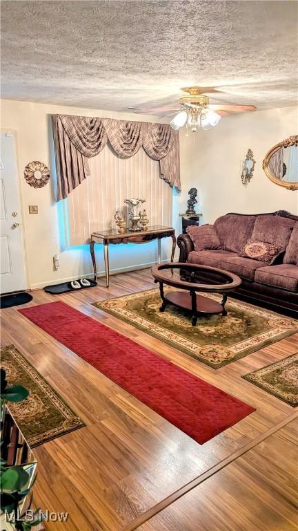 living room with ceiling fan, wood-type flooring, and a textured ceiling