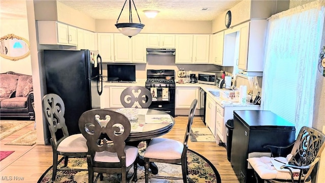 kitchen with white cabinetry, decorative light fixtures, light hardwood / wood-style floors, and black appliances