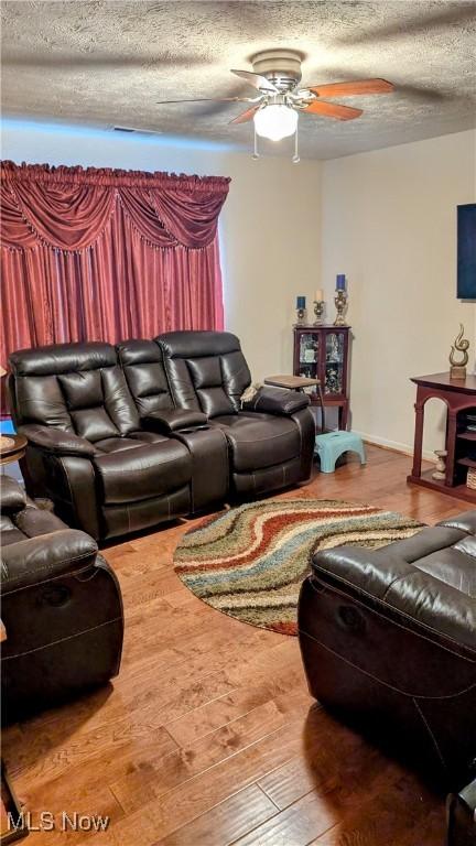 living room featuring ceiling fan, wood-type flooring, and a textured ceiling