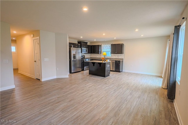 kitchen featuring a kitchen bar, a center island, light wood-type flooring, stainless steel appliances, and backsplash