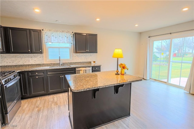 kitchen featuring a breakfast bar, sink, light stone counters, a center island, and stainless steel appliances