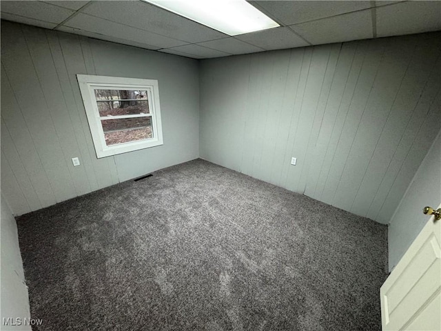 carpeted empty room featuring a drop ceiling and wood walls