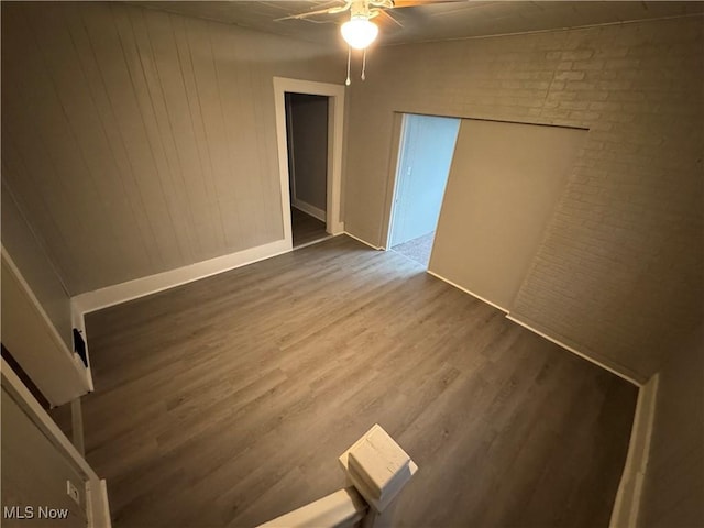 empty room featuring ceiling fan, brick wall, and wood-type flooring