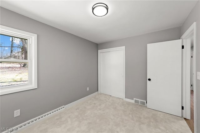 unfurnished bedroom with light carpet, a baseboard heating unit, and a closet