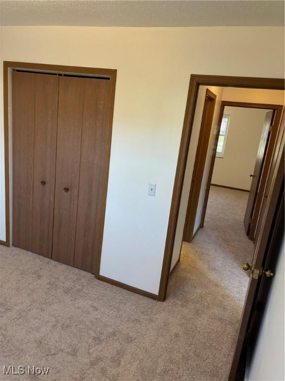 unfurnished bedroom with a closet, light carpet, and a textured ceiling