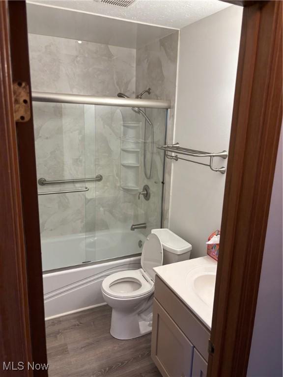 full bathroom featuring enclosed tub / shower combo, vanity, wood-type flooring, a textured ceiling, and toilet