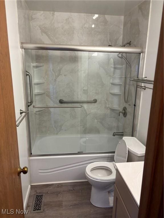 full bathroom with hardwood / wood-style flooring, vanity, bath / shower combo with glass door, and toilet