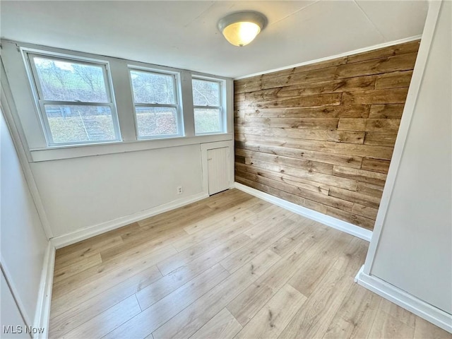 unfurnished room with light hardwood / wood-style flooring and wooden walls