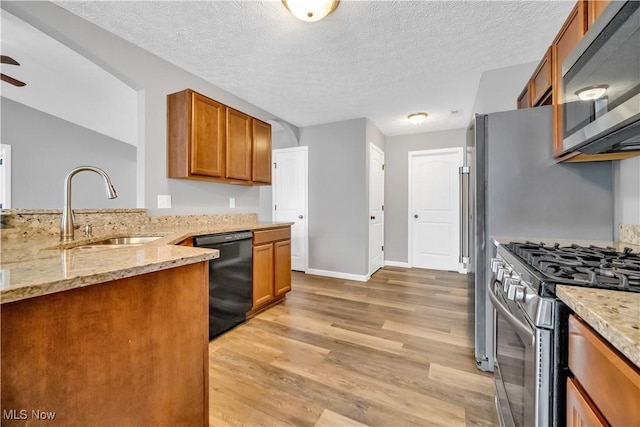 kitchen with sink, ceiling fan, appliances with stainless steel finishes, light stone counters, and light hardwood / wood-style floors