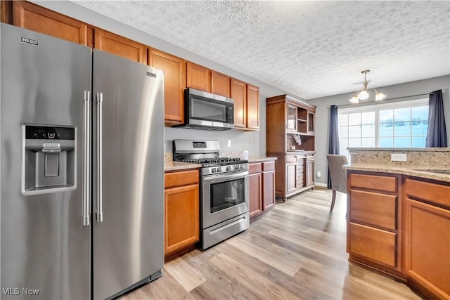 kitchen with decorative light fixtures, a notable chandelier, light stone counters, stainless steel appliances, and light hardwood / wood-style flooring