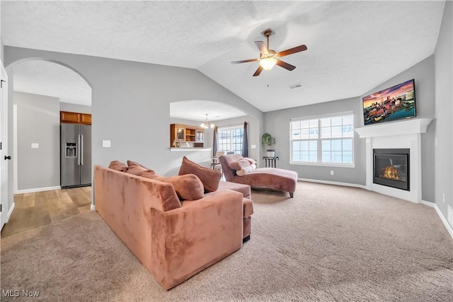 living room featuring lofted ceiling, ceiling fan with notable chandelier, light carpet, and a textured ceiling