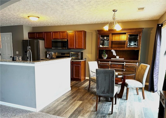 kitchen with an inviting chandelier, wood-type flooring, a textured ceiling, pendant lighting, and stainless steel appliances