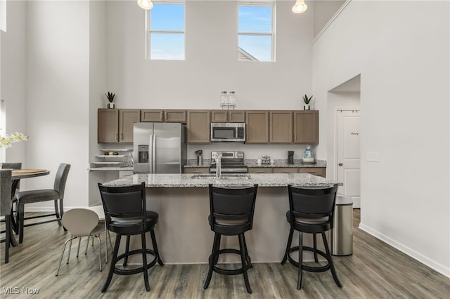 kitchen with a kitchen bar, a center island with sink, light stone countertops, and appliances with stainless steel finishes