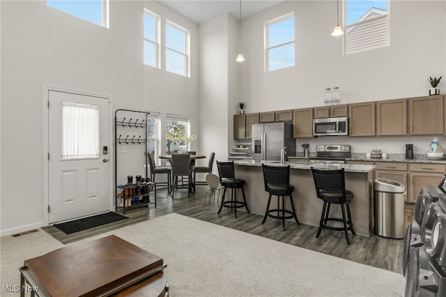 kitchen with an island with sink, a kitchen breakfast bar, hanging light fixtures, stainless steel appliances, and light stone countertops