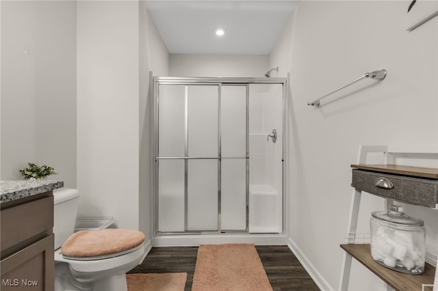 bathroom featuring vanity, wood-type flooring, a shower with shower door, and toilet