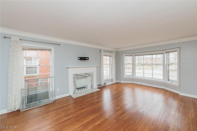 unfurnished living room with wood-type flooring, plenty of natural light, crown molding, and a high end fireplace