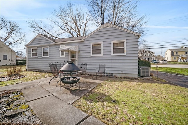 rear view of property featuring central AC unit, a fire pit, a patio, and a yard