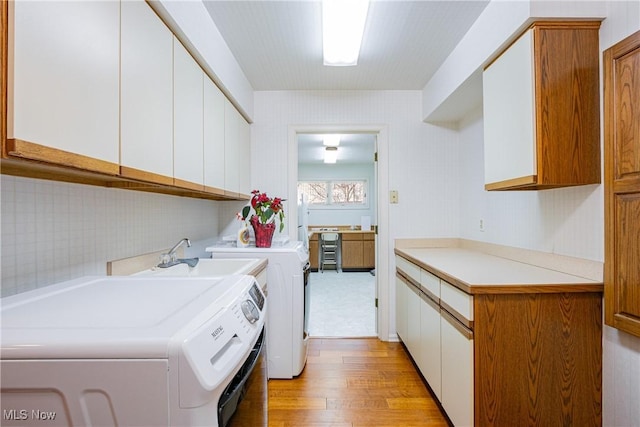 laundry room featuring cabinets, sink, light hardwood / wood-style flooring, and washing machine and clothes dryer