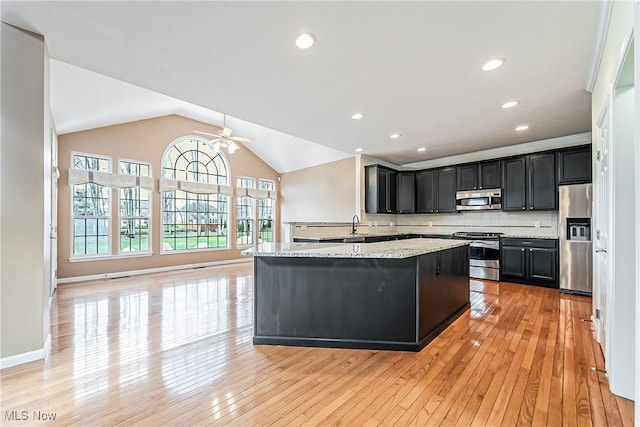 kitchen featuring a center island, appliances with stainless steel finishes, light stone countertops, and light wood-type flooring