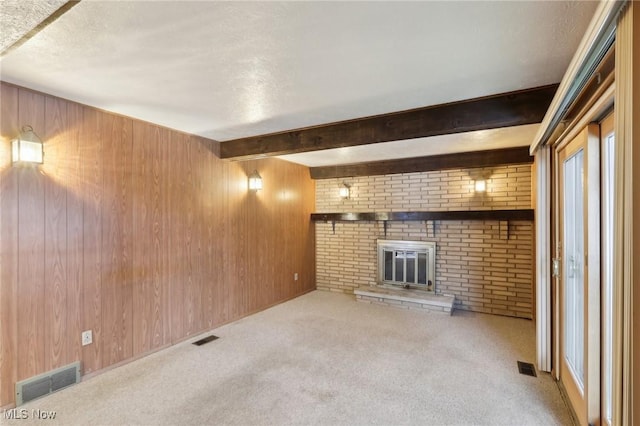 unfurnished living room with a fireplace, wood walls, beamed ceiling, light carpet, and a textured ceiling