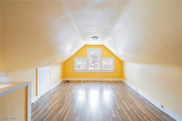 bonus room featuring hardwood / wood-style flooring, vaulted ceiling, and a textured ceiling