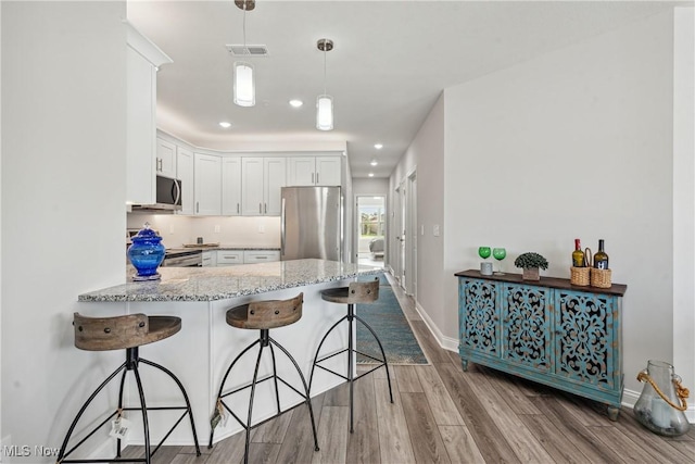 kitchen with a breakfast bar area, light hardwood / wood-style flooring, kitchen peninsula, stainless steel appliances, and white cabinets