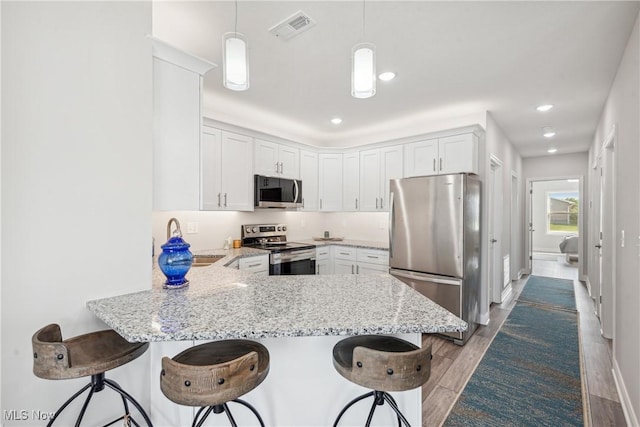 kitchen featuring a breakfast bar, white cabinets, hanging light fixtures, kitchen peninsula, and stainless steel appliances