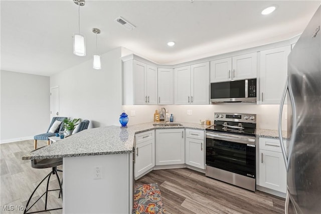 kitchen with sink, stainless steel appliances, white cabinets, a kitchen bar, and kitchen peninsula