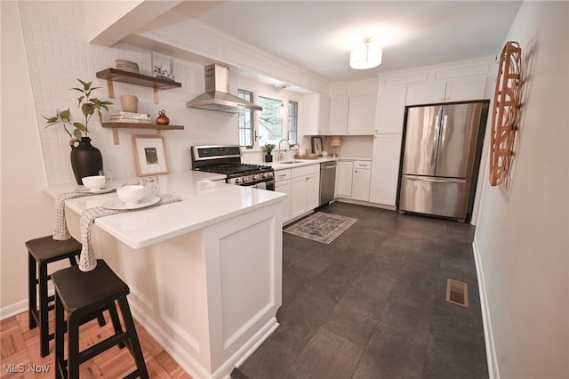 kitchen featuring white cabinetry, a kitchen breakfast bar, kitchen peninsula, stainless steel appliances, and wall chimney range hood